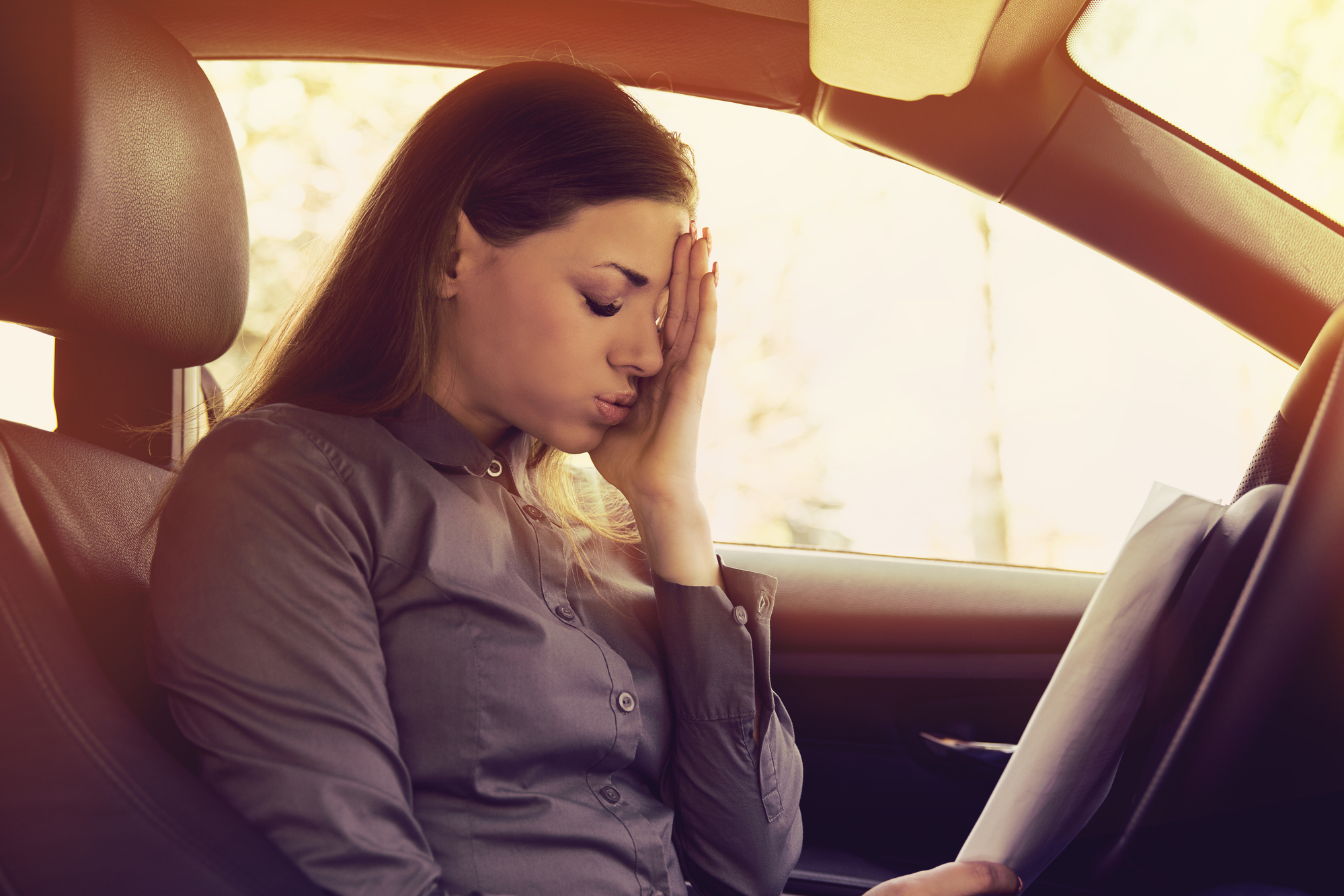 How To Avoid Drowsy Driving - Stressed woman driver with papers sitting inside her car